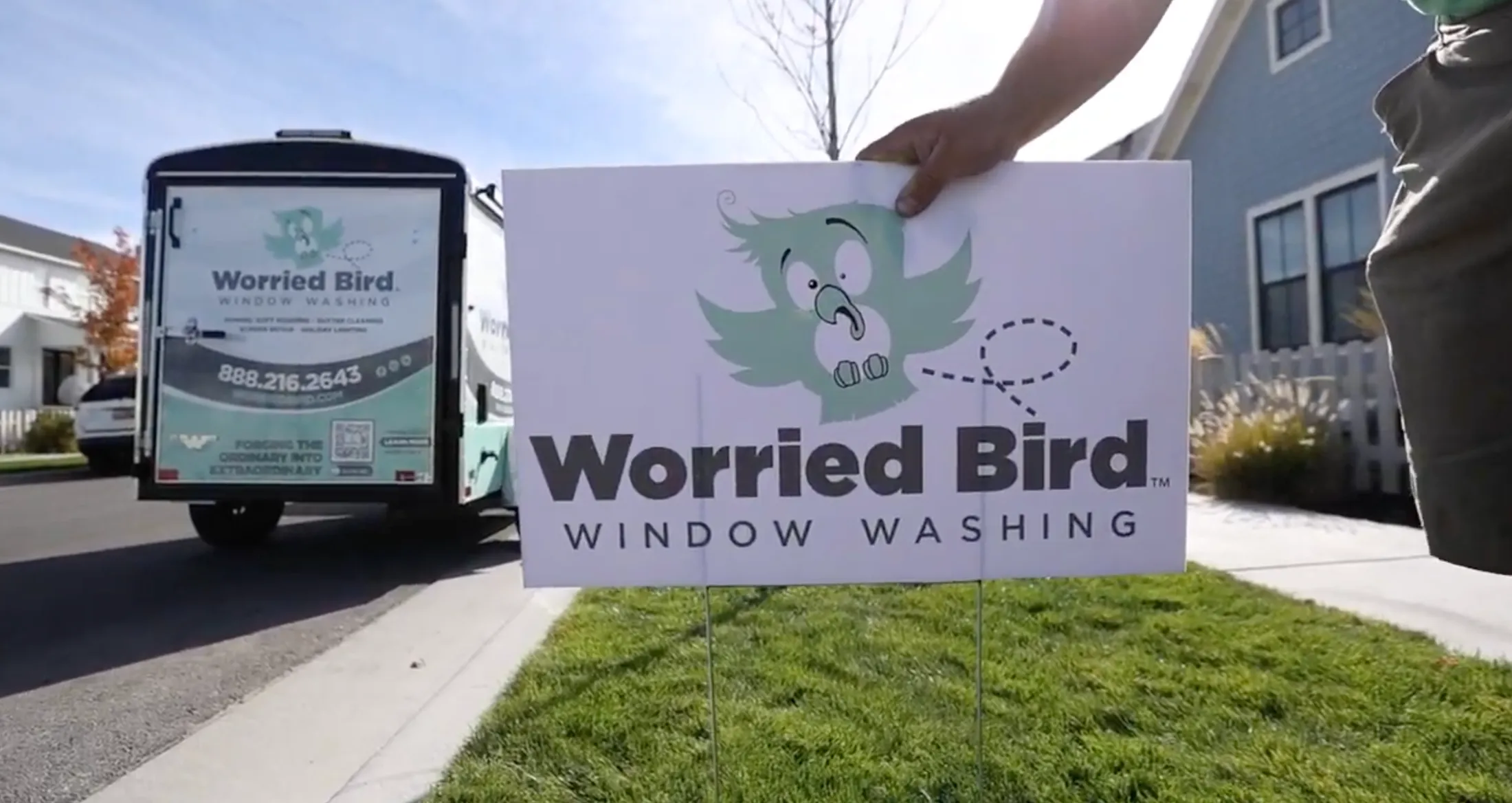 A Worried Bird yard sign standing on a home's lawn, with the branded trailer parked at the curb.
